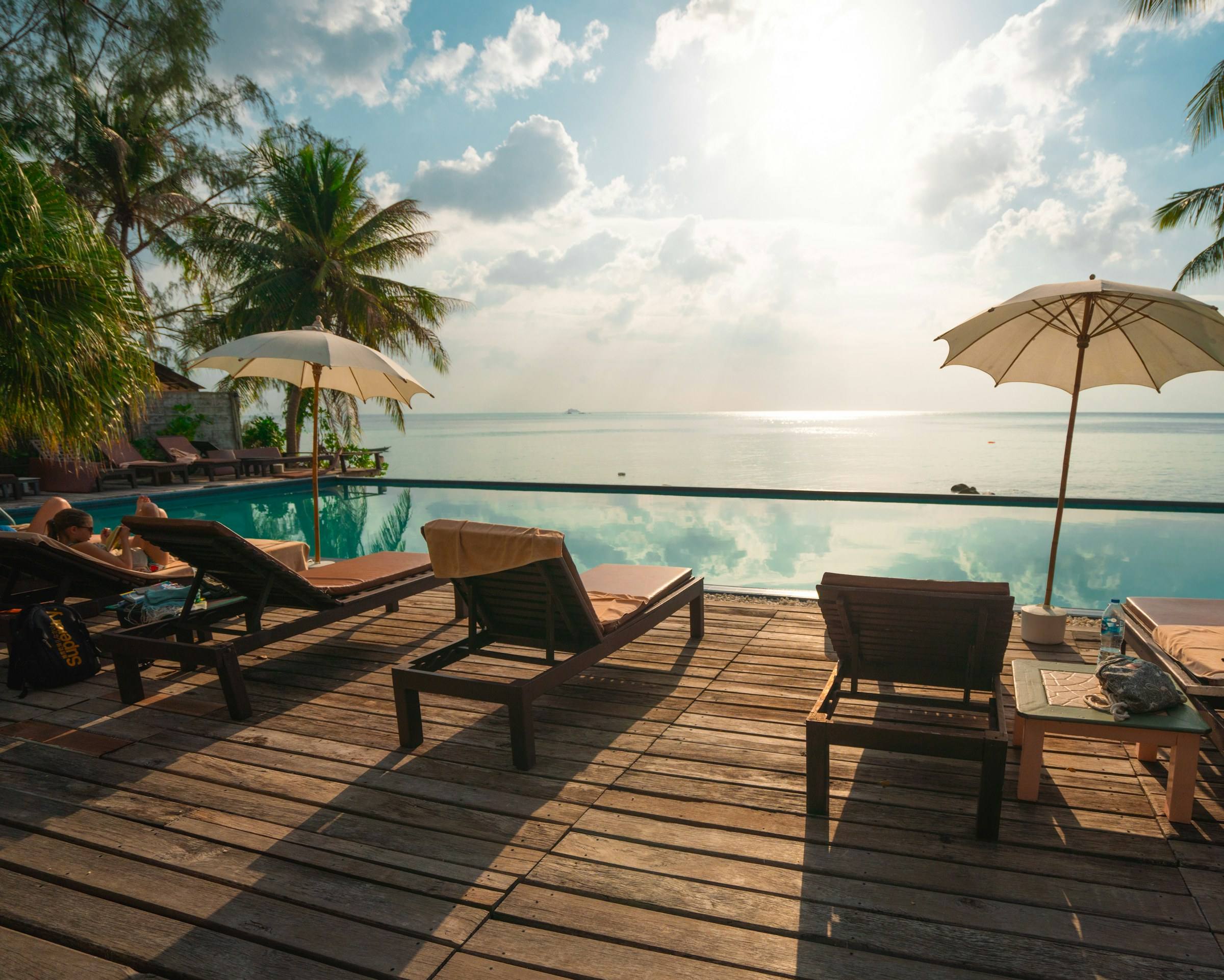 Resort pool deck with umbrellas and sun lounges overlooking the ocean at dusk