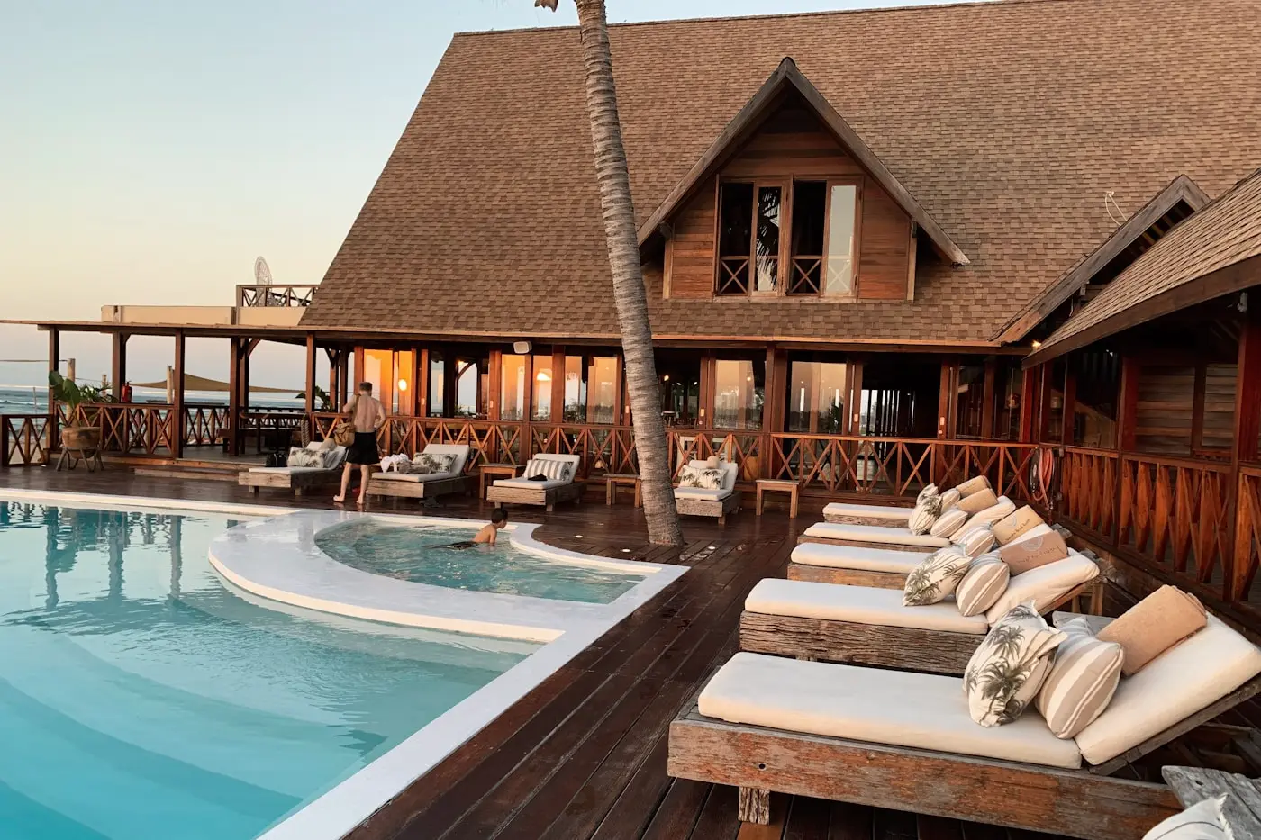 Beachfront resort pool deck with timber lodge and sun lounges at dusk