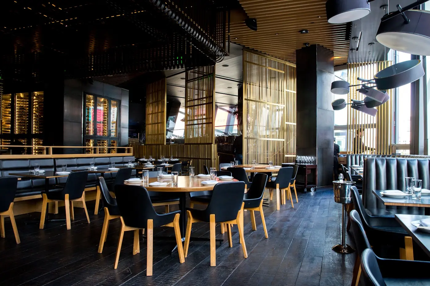 Contemporary restaurant interior in dark timber and brass, tables set for service